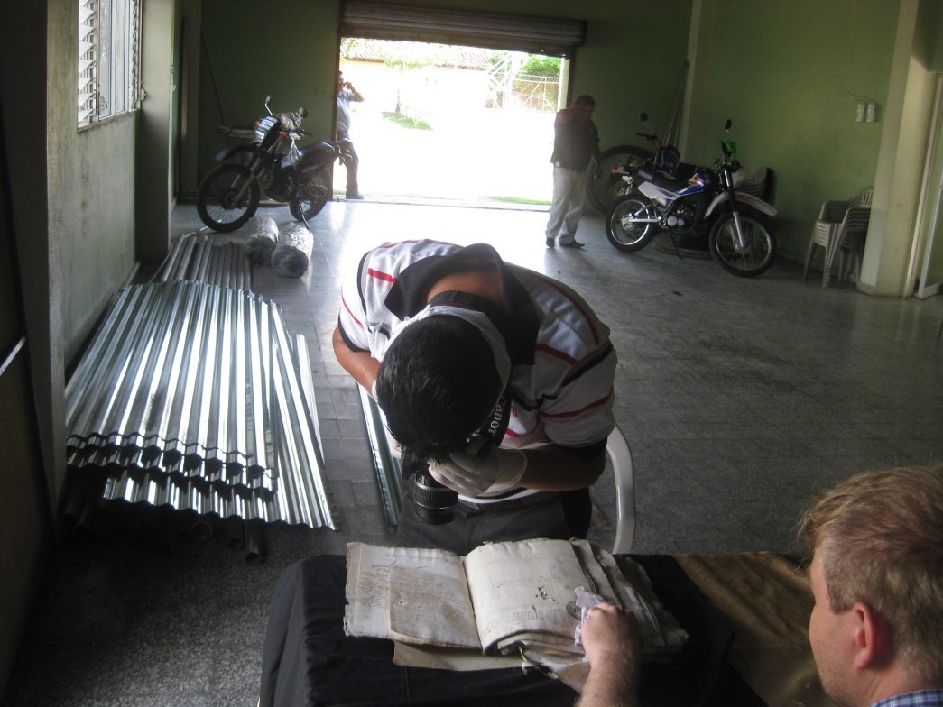 Miguel Girón, con guantes y una cámara réflex, fotografía un libro de actas abierto sobre una mesa, en el zaguán de la alcaldía